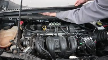 Tamirci arabanın kaputunu açar ve motoru ortaya çıkarır..