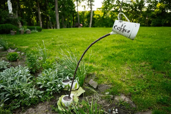 Yeşil bitkiler ve çimlerle çevrili bir kahve temalı sanatsal bahçe kurulumu.