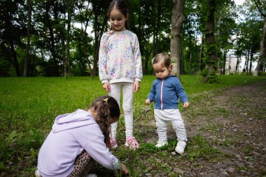 Üç çocuk birlikte dışarıda güzel yeşil bir park ortamında vakit geçiriyorlar.