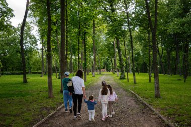 Aydınlık ve aydınlık bir günde ağaçlık bir park yolunda yürüyen bir aile..