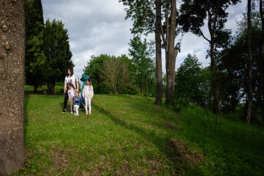 Güneşin altındaki yeşil bir parkta ferahlatıcı bir yürüyüşün tadını çıkaran bir aile..