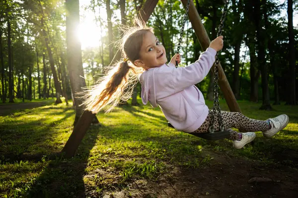 Mutlu bir kız altın güneş ışığıyla aydınlatılmış bir ormanda sallanmaktan hoşlanır..