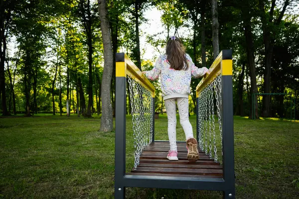 Gün batımında uzun yeşil ağaçlarla çevrili bir park köprüsünü keşfeden küçük bir çocuk.