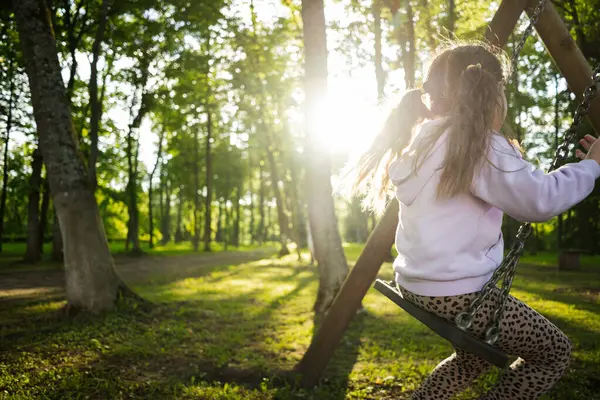Uzun ağaçlarla çevrili sakin bir parkta sallanan bir çocuk.