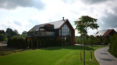 Geniş yeşil çimenleri, patikası ve bulutlu bir gökyüzünün altında yemyeşil ağaçları olan çarpıcı çağdaş bir ev..