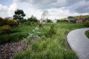Yolları, yeşil bitkileri ve bulutların altındaki binaları barındıran sakin bir bahçe..