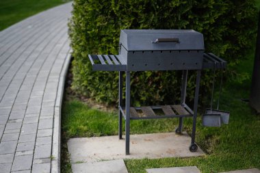 Metal barbekü ızgarası bir patika ve çalıların yakınındaki çimlerin üzerine yerleştirilmiş.