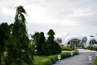 Canlı peyzaj ile çevrili beyaz kubbe şekilli modern bir bina.