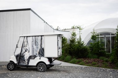 Çağdaş bir binanın yanında, yemyeşil bir çevresi olan elektrikli golf arabası..