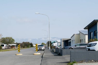 Akranes, İzlanda - 15 Haziran 2025: Akranes içinde konut evleri, park edilmiş arabalar ve manzaralı tepeleri gösteren bir yol.