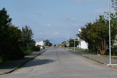 Akranes 'te, mavi gökyüzünün altındaki yeşil ve uzak dağların çerçevelediği huzurlu bir cadde.
