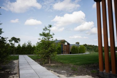 Ağaçlar, patika ve zarif bir ev tasarımı içeren güzel bir kırsal çevre.