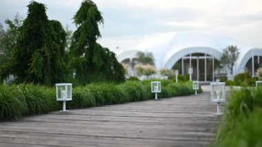 Modern fenerler ve yemyeşil yemyeşil ile zarif ahşap patika beyaz bir olay çadırına hoş geldin girişi sağlar..