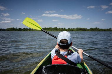 Güneşli bir günde huzurlu bir gölde kano süren bir çocuk.