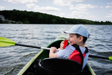 Doğayla çevrili sakin bir gölde kayak yaparken can yeleği giyen bir çocuk.