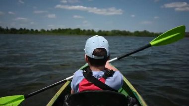 Genç bir çocuk güneşli bir günde sakin bir gölde güvenli bir şekilde kürek çeker..