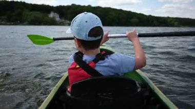 Genç bir çocuk güzel bir yaz gününde dingin bir gölde kanoyla yüzer..