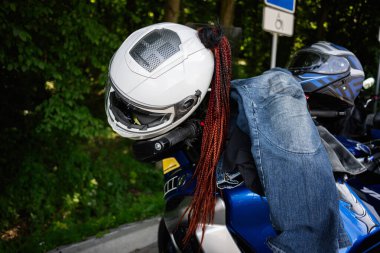 Yeşil yapraklarla çevrili park halindeki bir motosiklette dinlenen kask ve ceket..