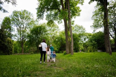 Aile, dingin yeşil ve uzun ağaçlarla dolu huzurlu bir parkta yürüyüş yapıyor.