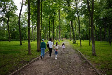 Bir grup insan yeşil bir orman parkında yol boyunca yürüyor.