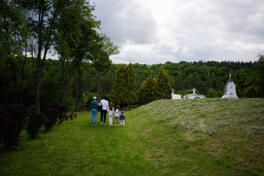 Bir aile, ağaçlarla ve çimenli yollarla dolu huzurlu bir parkta birlikte yürüyor.