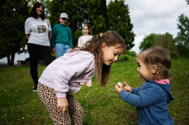 Yeşillik ve aile üyeleriyle çevrili açık havada eğlenen çocuklar..