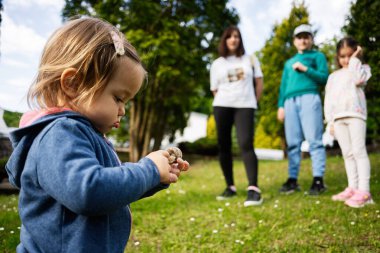 Başkaları bulanık arkaplanda dururken, bir çocuk ilginç bir şekilde bir nesneyi inceler..