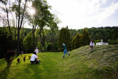Çocuklar çimenli bir tepede oynarken bir yetişkin dışarıda değerli anları yakalıyor.