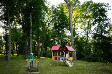 Güneşli bir günde parkta oyun alanı ve ağaçlar.
