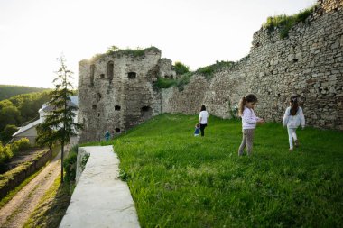Çocuklar güneşli gökyüzünün altında, yemyeşil yemyeşil harabelerle çevrili antik şato harabelerinde oynuyorlar..