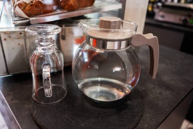 Cam sürahi ve ters çevrilmiş bardak servis tezgahında, fırınlanmış malların yanında.