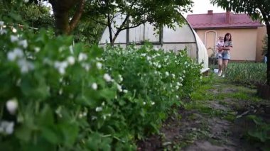 Bir anne, canlı evlerinin bahçesinde yürürken küçük çocuğunu nazikçe taşır..