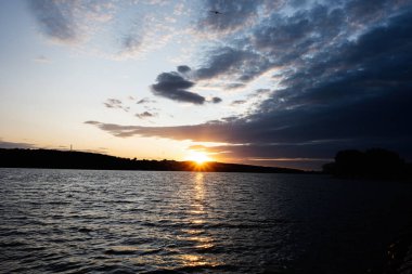 Sakin göl, canlı bir günbatımı ve dağılmış bulutlar suya yansıyor..