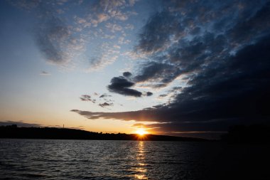 Sakin bir göl üzerinde gün batımı sahnesi, canlı bulutlar ve huzurlu bir atmosfer sergiliyor..