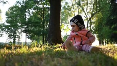 Tatlı küçük bebek güneşli bir parkta yeşil çimlerin üzerinde oturarak eğleniyor..