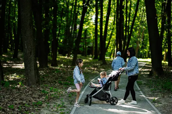 Ağaçlar ve güneş ışığıyla çevrili bir parkta birlikte yürüyen bir anne.