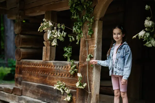 Genç bir kız yeşillik içinde kırsal bir ahşap binanın yanında poz veriyor..