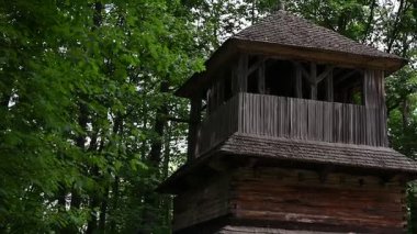 Kırsal ahşap çan kulesi yemyeşil ormanın ortasında duruyor, eski çanları çalıyor..