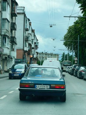 Kyiv, Ukrayna - 24 Haziran 2025: Ford Granada. Bulutlu bir gökyüzünün altında yol, park edilmiş arabalar ve eski mimarinin yer aldığı bir şehir manzarası..