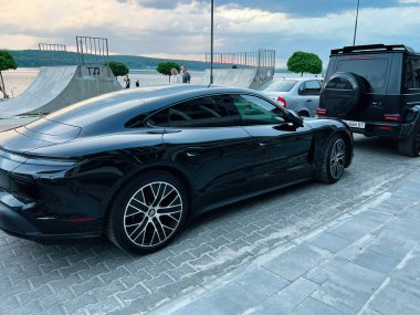 Kyiv, Ukrayna - 24 Haziran 2025: Pahalı bir akşam gökyüzünün altında nehir kenarına park edilmiş lüks araçlar. Porsche Taycan 4S Performans. 