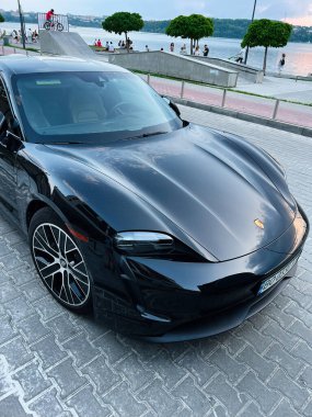 Kyiv, Ukrayna - 24 Haziran 2025: Parlak siyah spor Porsche Taycan 4S Performans arabası sakin bir akşamda göl kenarında sergilendi.