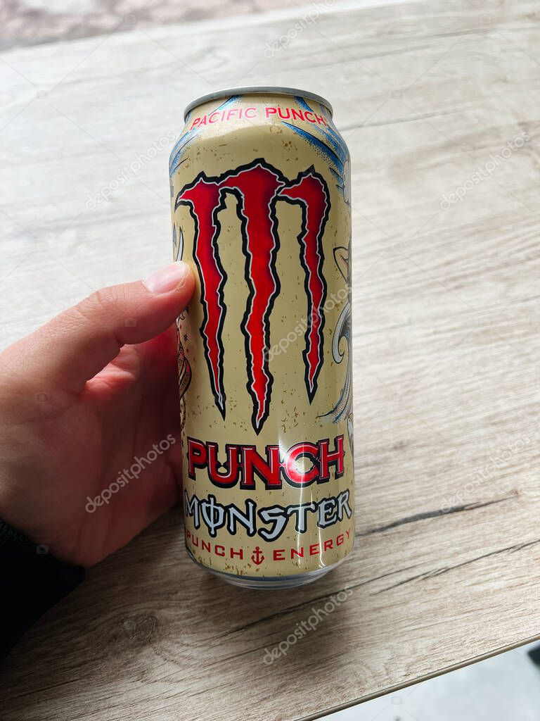 Kyiv, Ukraine - June 24, 2025: Person holding a branded Monster Punch energy drink can against a natural wooden background