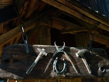 Kırsal ahşap çatının altında zincirli antika demirci aletleri sergileniyor.
