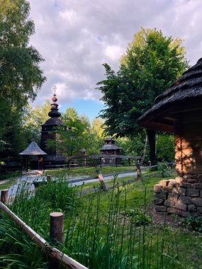 Güneşli bir günde geleneksel mimarinin sergilendiği, yeşilliklerin arasına yerleşmiş ahşap bir Ukrayna kilisesi..