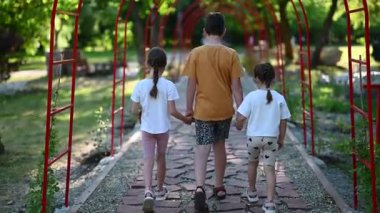 Küçük çocuklar güzel bir parkta birlikte yürüyor, dışarıda kaygısız bir yaz gününün tadını çıkarıyorlar..