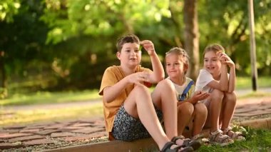 Neşeli çocuklar çimlerin üzerinde birlikte oturur, parkta güneşli güzel bir günün tadını çıkarırlar..