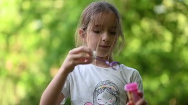 Neşeli genç kız canlı yeşil park ortamında narin sabun köpükleri üflerken eğleniyor..