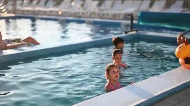 Neşeli çocuklar açık havuzda su sıçratarak ve yüzerek eğleniyorlar..