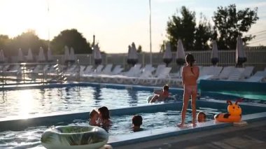 Çocuklar ve yetişkinler güneşli bir yüzme havuzunda eğleniyorlar, yaz tatilinin tadını çıkarıyorlar..