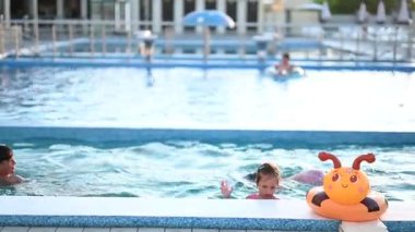 Çocuklar ve aile ferahlatıcı yaz eğlencesinin tadını çıkarıyor, yüzüyor ve havuzda mutlu mesut oynuyorlar..
